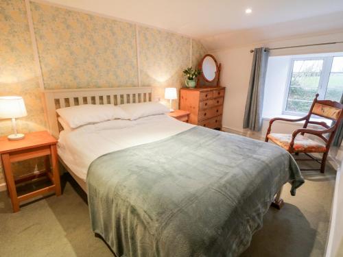a bedroom with a bed and a chair and a window at 2 Rose Cottages in Looe