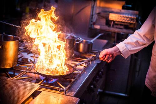 a person cooking food in a pan on a stove at Landgasthof Brunnenwirt Zum Meenzer in Fischbachtal