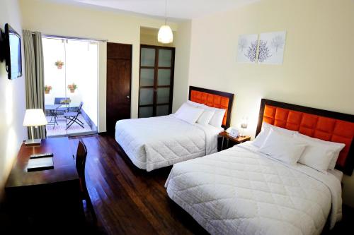 a bedroom with two beds and a desk and a window at Mint Hotel in Arequipa