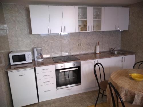 eine Küche mit weißen Schränken, einem Tisch und einer Mikrowelle in der Unterkunft Apartment Vojinovic in Aranđelovac