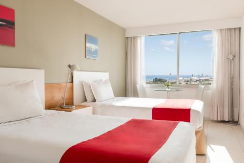 two beds in a hotel room with a view of the ocean at UY Proa Sur Hotel in La Paloma