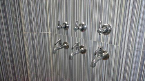 a group of silver faucets on a bathroom wall at Nature's Paradise Homestay in Haridwār