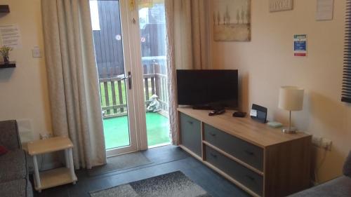 a room with a desk with a television and a balcony at D&D Holiday Chalet in Bridlington