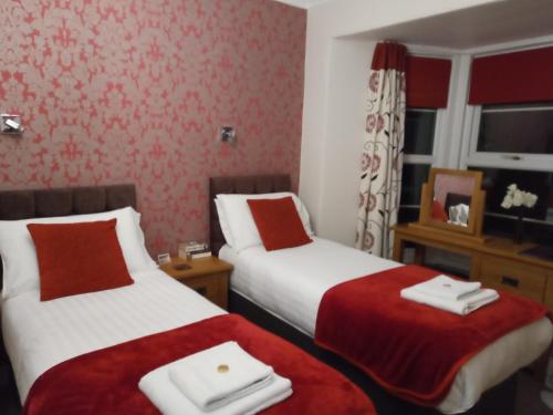 two beds in a hotel room with red wallpaper at Lawnswood Guest House in Torquay