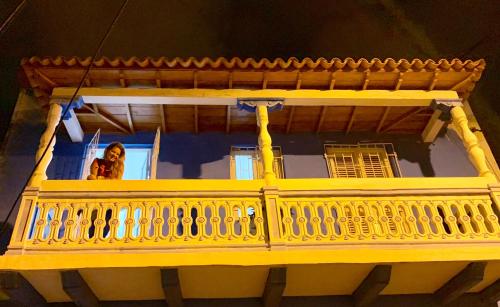 a woman standing on the balcony of a yellow building at Casa de la Cruz in Cartagena de Indias