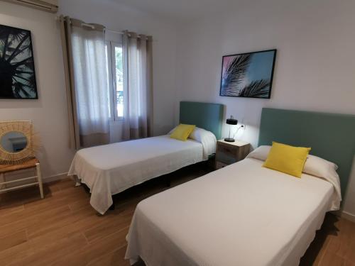 Villa Bahía في بورت دي بوينسا: سريرين في غرفة مع وسائد بيضاء وصفراء