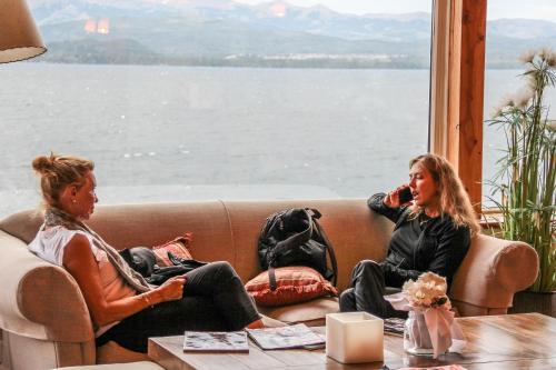 two women sitting on a couch looking out a window at Sol del Nahuel - Hotel & Spa in San Carlos de Bariloche