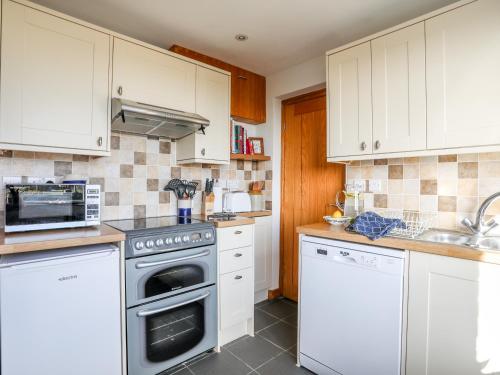 a kitchen with white cabinets and a stove top oven at Yr Orsedd in Holyhead