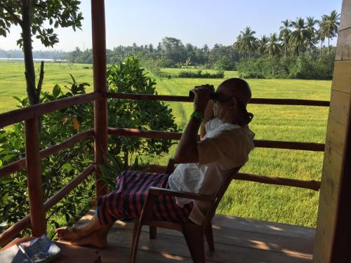 a woman sitting on a porch taking a picture of a field at lake paradise cabana in Tissamaharama
