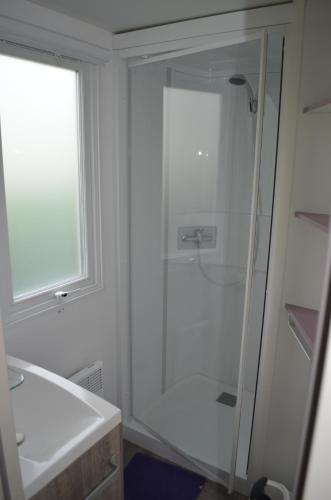 ein weißes Bad mit einer Dusche und einem Waschbecken in der Unterkunft Camping La Venise Du Bocage in Nesmy