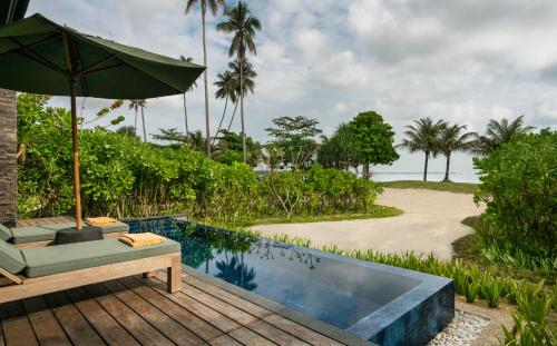 The Residence Bintan في Kawal: فناء فيه مظلة ومسبح بجانب شاطئ