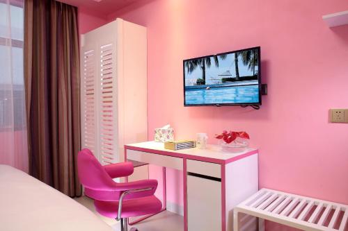 a pink room with a desk and a tv on a wall at Care Hotel Coast Collection in Sanya