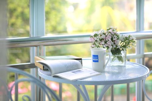 una mesa con un libro y una taza de café y flores en Care Hotel Coast Collection, en Sanya