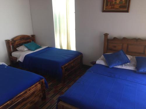 three beds in a room with blue sheets at Hotel Casa Floralia in Tibasosa