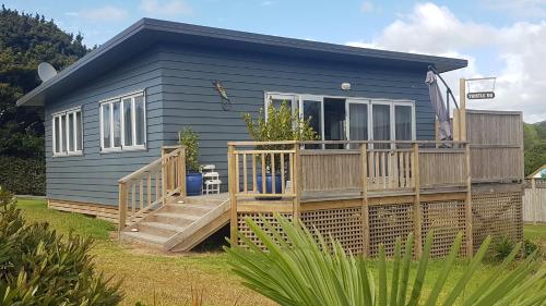 a blue tiny house with a large deck at Thistle Do Beach Bach in Ruakaka