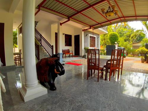 eine Kuh, die mitten auf einer Veranda mit einem Tisch und Stühlen steht in der Unterkunft Radha Tourist Home in Polonnaruwa
