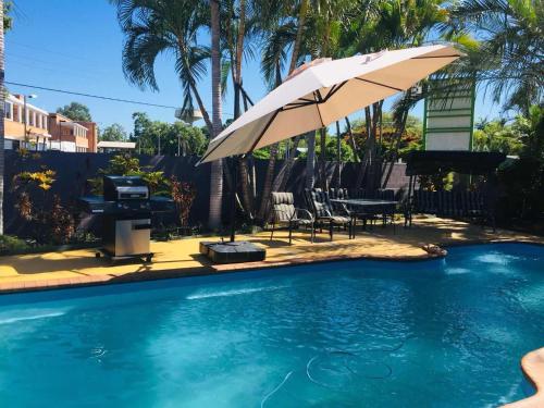 a pool with an umbrella and a table and a piano at Emerald Highlands Motel in Emerald