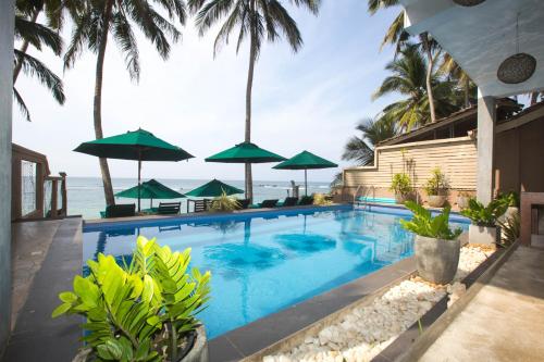 a swimming pool with green umbrellas and the ocean at Sea World Boutique Hotel in Mirissa