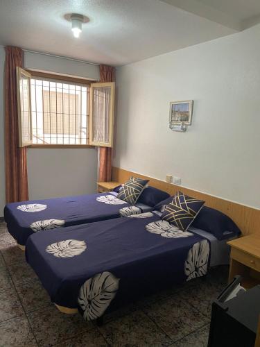 a room with two beds with blue sheets and a window at Hotel Arce in San Pedro del Pinatar