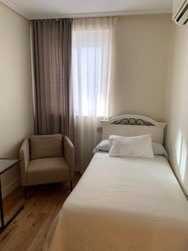 a bedroom with a bed and a chair and a window at Hotel Boutique Astorga in Valladolid