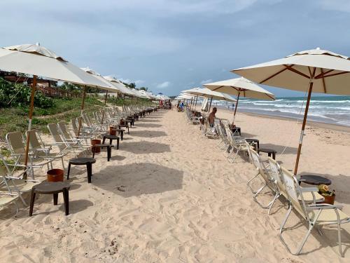 uma fila de cadeiras e guarda-sóis numa praia em Flat Extraordinário Beira Mar em Porto de Galinhas com pé na areia Cupe Beach Living em Porto de Galinhas