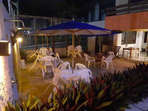 a patio with white chairs and a blue umbrella at Hotel Enseada de Ponta Negra in Natal