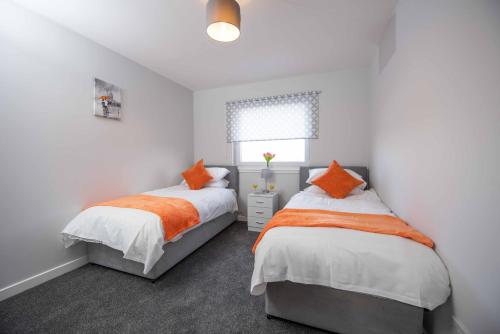 2 bedden in een slaapkamer met witte muren en oranje kussens bij PREMIER - Wishaw En-Suite Apartment in Wishaw