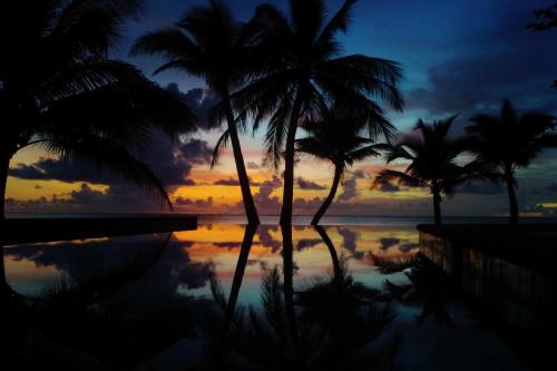 a view of a pool with palm trees and a sunset at Romantic Beach Villas in General Luna