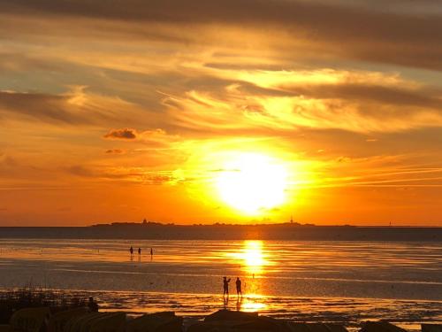 a sunset at the beach with people walking on the beach at Haus zur Heimat in Cuxhaven