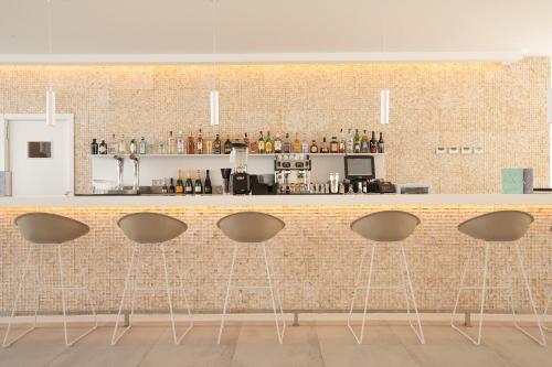 a bar with four stools in front of a brick wall at Hotel Anfora Ibiza in Es Cana