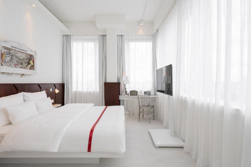 a white bedroom with a bed and a desk at Ruby Leni Hotel Dusseldorf in Düsseldorf