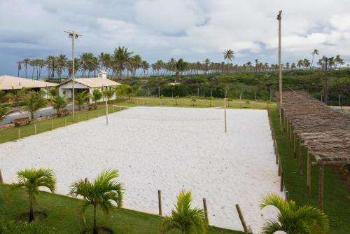 an empty volleyball court with palm trees and the ocean at Tree Bies Resort - Oficial in Subaúma