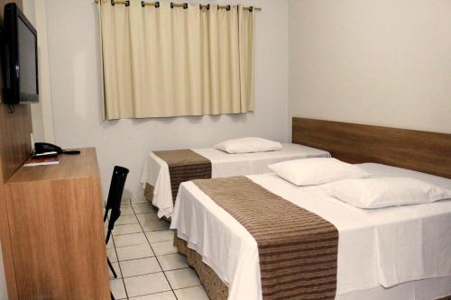 a hotel room with two beds and a desk at Abudi Hotel in Cuiabá