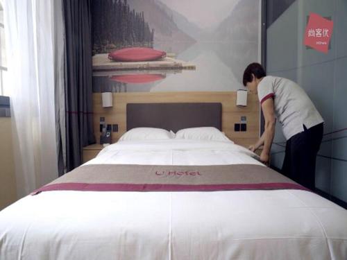 a woman standing next to a large bed at Thank Inn Chain Hotel anhui bengbu huaishang district mohekou county in Bengbu