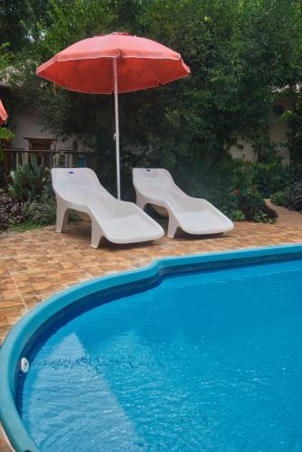 a red umbrella and two chairs and a swimming pool at Vacaciones Aregua CASA VANESSA in Areguá