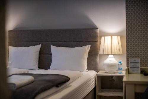 a bed with white pillows and a table with a lamp at So&sol boutique Hotel, Tuzla in Tuzla