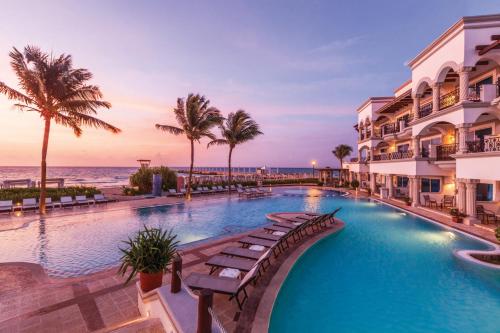 a resort pool with palm trees and the ocean at Hilton Playa del Carmen, an All-Inclusive Adult Only Resort in Playa del Carmen