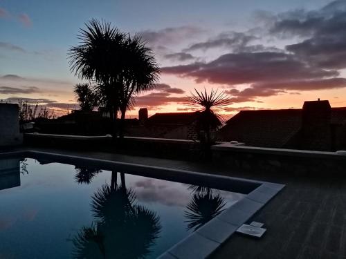 a sunset over a swimming pool with palm trees at GRANARY'S HOUSE in Sete Cidades