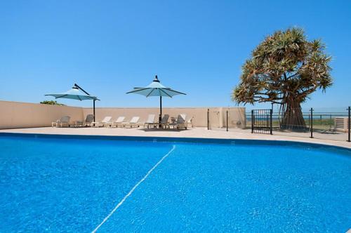 a blue swimming pool with chairs and umbrellas at Beachside Tower Apartments in Gold Coast