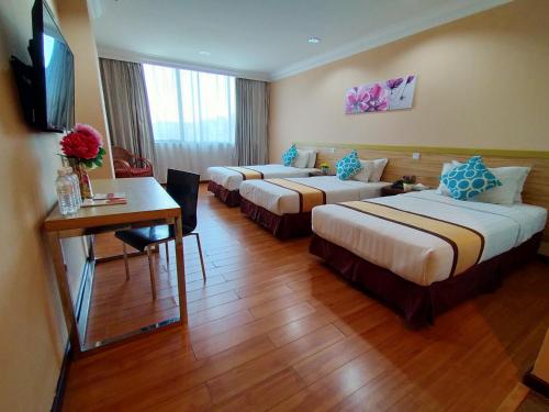 Habitación de hotel con 3 camas, escritorio y TV. en TD Plaza Hotel, en Kota Kinabalu
