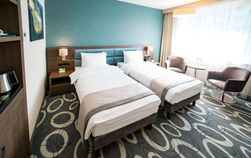 a hotel room with two beds and a chair at Holiday Inn Dąbrowa Górnicza-Katowice by IHG in Dąbrowa Górnicza