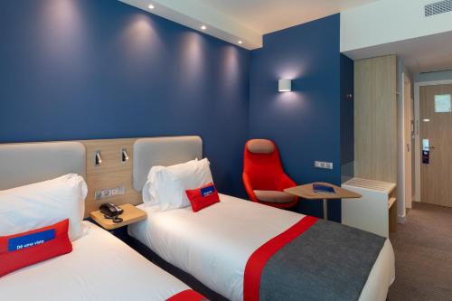 a hotel room with two beds and a red chair at Holiday Inn Express - Lisbon - Plaza Saldanha by IHG in Lisbon