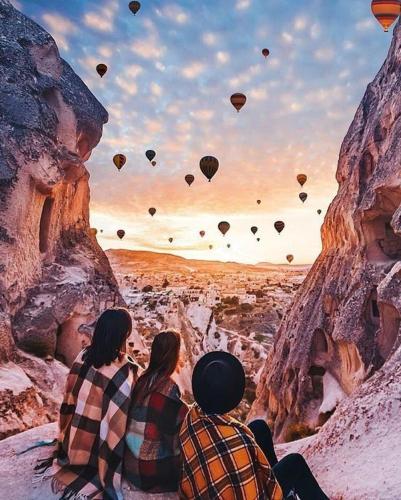 two people sitting on a cliff watching hot air balloons at Elaa Cave Hotel in Ortahisar