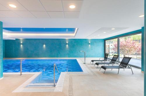 a swimming pool with black chairs and a blue wall at Wellness Hotel Panorama in Trenčianske Teplice