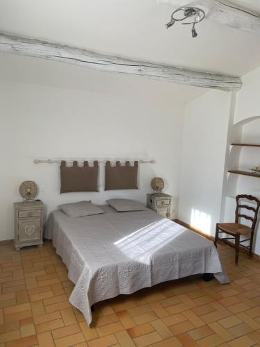 a white bedroom with a bed and a chair at Maison La Plaine in Lourmarin