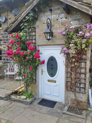 a stone house with a white door and pink flowers at Hawkshead Cottage in Glossop