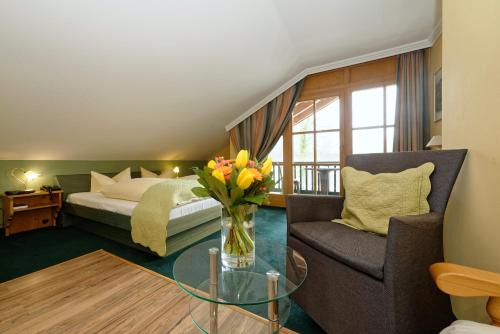 a bedroom with a bed and a vase of flowers and a chair at Hotel zum Maximilian in Bad Feilnbach