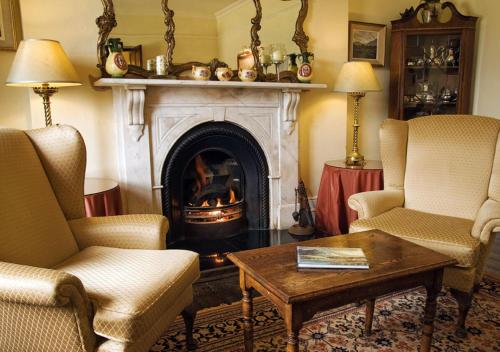 a living room with a fireplace with two chairs and a table at Lough Inagh Lodge Hotel in Recess
