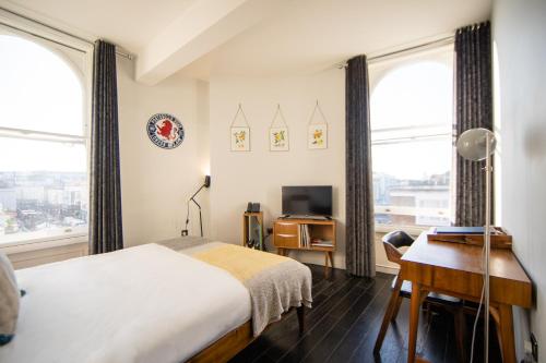 een slaapkamer met een bed, een bureau en ramen bij The Distillery in Londen