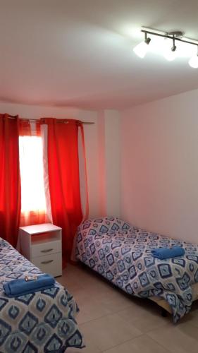 1 dormitorio con 2 camas y una ventana con cortinas rojas en Departamento amoblado de un dormitorio 43m2 en Río Grande